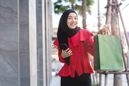 happy face muslim woman in red dress holding shopping bag and walking outdoor street. Concept people activity in shopping festival season christmas and new year.の写真素材