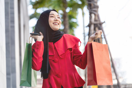 happy face muslim woman in red dress holding shopping bag and walking outdoor street. Concept people activity in shopping festival season christmas and new year.の写真素材