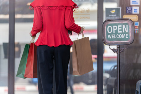 woman in red dress holding shopping bag and walking to shop building. Concept people activity in shopping festival season christmas and new year.の写真素材