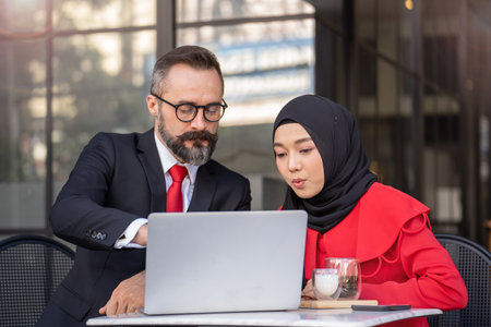 senior man in smart business suit talking to islam woman at outdoor coffee table. Concept business presentation with technology laptop device.の写真素材