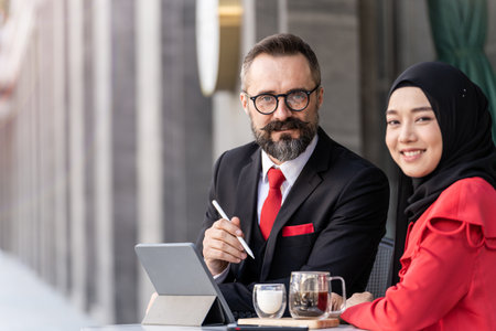 senior man in smart business suit talking to islam woman at outdoor coffee table. Concept business presentation with technology laptop device.の写真素材