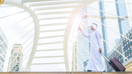 arab man carry a suitcase at business city walk in the business landmark city with the modern steel structure and exterior wall modern buildingの写真素材