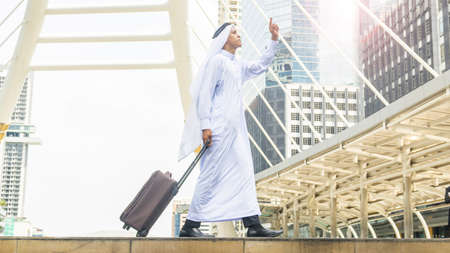 arab man carry a suitcase at business city walk in the business landmark city with the modern steel structure and exterior wall modern buildingの写真素材