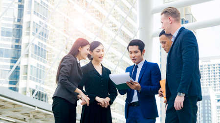team of business multi internationality people smart man and woman talk and present the project work with the paper work on the hand  in good feeling at outdoor pedestrian walk way the city space modern buildingの写真素材