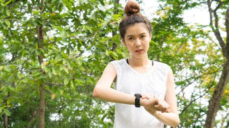 Asian cute healthy fit and firm slim teen lady look at the smartwatch to set GPS or heart rate before running and workout  at outdoor garden parkの写真素材