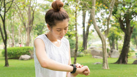 Asian cute healthy fit and firm slim teen lady look at the smartwatch to set GPS or heart rate before running and workout  at outdoor garden parkの写真素材