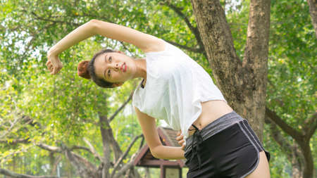 Asian cute healthy fit and firm slim teen lady warm up before workout for weight training or running at outdoor garden parkの写真素材