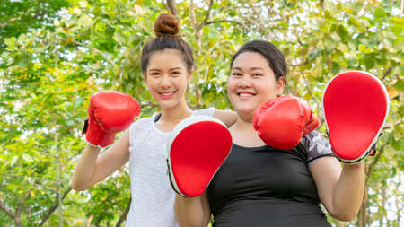 Fat woman dieting with fit cute girl fitness and training warm up and boxing at outdoor park garden.の写真素材