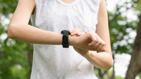 Asian cute healthy fit and firm slim teen lady look at the smartwatch to set GPS or heart rate before running and workout  at outdoor garden parkの写真素材