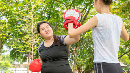Fat woman dieting with fit cute girl fitness and training warm up and boxing at outdoor park garden.の写真素材