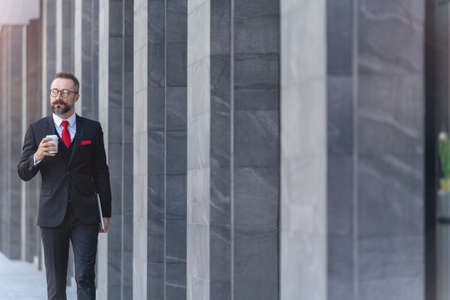 Manager senior man in business suit holding cup of coffee and laptop notebook. business lifestyle in coffee time at morning daylight.man feeling fresh and happy with confident of success.の写真素材