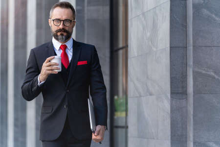 Manager senior man in business suit holding cup of coffee and laptop notebook. business lifestyle in coffee time at morning daylight.man feeling fresh and happy with confident of success.の写真素材