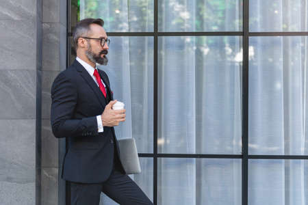 Manager senior man in business suit holding cup of coffee and laptop notebook. business lifestyle in coffee time at morning daylight.man feeling fresh and happy with confident of success.の写真素材