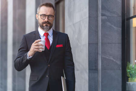 Manager senior man in business suit holding cup of coffee and laptop notebook. business lifestyle in coffee time at morning daylight.man feeling fresh and happy with confident of success.の写真素材