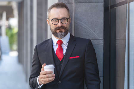 Manager senior man in business suit holding cup of coffee and laptop notebook. business lifestyle in coffee time at morning daylight.man feeling fresh and happy with confident of success.の写真素材