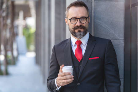 Manager senior man in business suit holding cup of coffee and laptop notebook. business lifestyle in coffee time at morning daylight.man feeling fresh and happy with confident of success.の写真素材