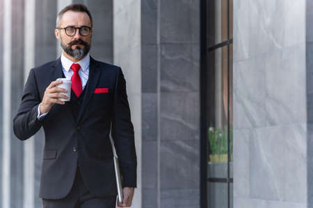 Manager senior man in business suit holding cup of coffee and laptop notebook. business lifestyle in coffee time at morning daylight.man feeling fresh and happy with confident of success.の写真素材