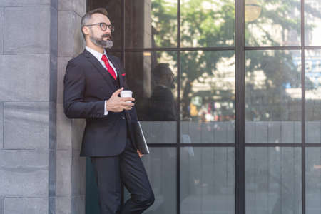 Manager senior man in business suit holding cup of coffee and laptop notebook. business lifestyle in coffee time at morning daylight.man feeling fresh and happy with confident of success.の写真素材