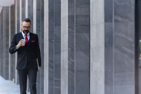 Manager senior man in business suit holding cup of coffee and laptop notebook. business lifestyle in coffee time at morning daylight.man feeling fresh and happy with confident of success.の写真素材