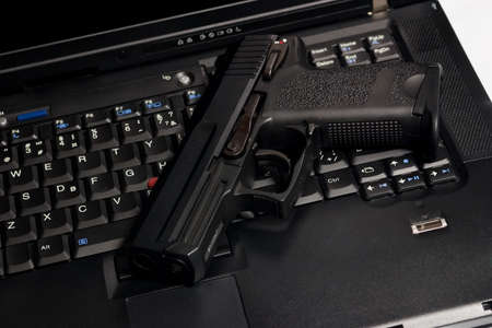 Black pistol on the keyboard of laptopの写真素材