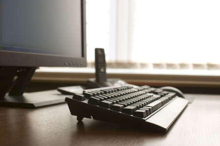 Modern workplace. Competer keyboard, tft monitor and DECT telephone on a wood desk.の写真素材