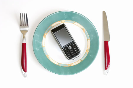 Modern cellular phone (smartphone) on a dish, in surroundings a knife and forkの写真素材