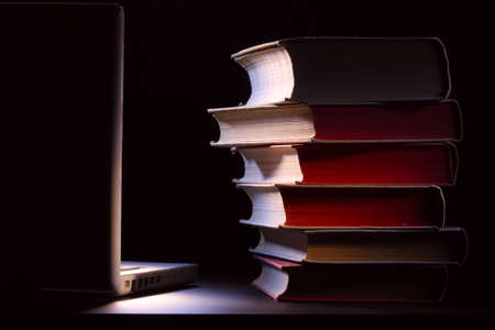 Old books and laptop on a table. Black backround.の写真素材