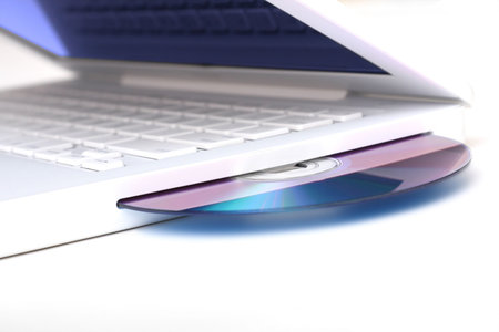 White laptop with optical disk in slot-loading drive.