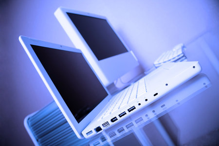 Blue tint modern elegance white laptop and  computer on a glass desk.