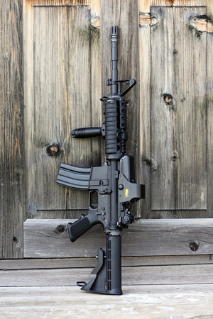 The Black Rifle. 14,5" AR-15 assault carbine (M4A1) with holographic sight against an old wooden door. Vertical composition.のeditorial素材