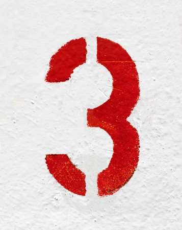 Red stenciled number Three on old painted wall の写真素材