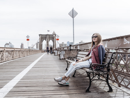 New York, USA - September 21, 2015: The woman is sitting on a bench on the Brooklyn Bridge and looking at skyscrapers of New York.のeditorial素材