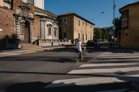 Milan, Italy - August 11, 2016: Italian woman in a white dress rides a bike in the morning to work on a sunny street in Milan, Italy.のeditorial素材