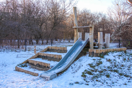 A wooden slide sits on a snowy playground surrounded by trees, inviting children to play on a crisp winter day.の写真素材