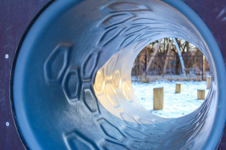 A playground tunnel gives a unique view of the snowy landscape, framed by wooden posts that enhance the tranquil winter vibe.の写真素材
