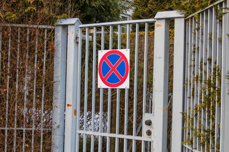 A no parking sign is prominently displayed on a metal gate in a residential area, surrounded by lush greenery and trees.の写真素材