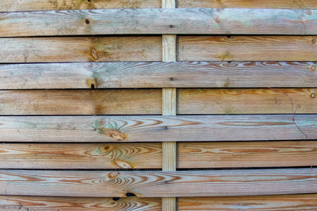 Close-up of a rustic wooden fence featuring slats with varied grain patterns, showing warm, natural tones and textures in daylight.の写真素材
