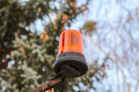 Bright orange warning light sits on a pole against a backdrop of snowy trees outdoors, signaling...