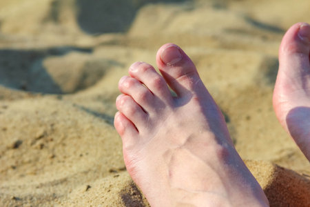 Woman's bare feet relaxing on warm sandy beach during peaceful summer vacationの写真素材