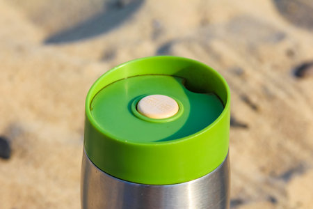 Green camping lantern sitting on sandy beach surface with natural lighting effectの写真素材