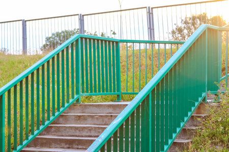 Green metal pedestrian bridge with concrete steps leading over railway tracks in urban areaの写真素材