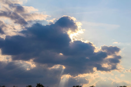 Dramatic evening sky with golden sunlight breaking through dark storm clouds creating atmospheric...