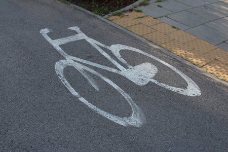 White bicycle symbol painted on dark asphalt road surface indicating cycling lane and urban transportation infrastructureの写真素材