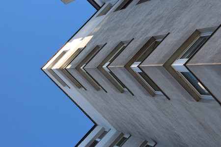 Low angle view of modern white residential building with balconies against clear blue sky emphasizing architectural heightの写真素材