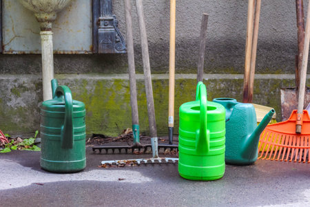 Garden storage corner with collection of watering cans and tools hanging in organized outdoor...