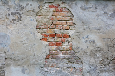 Weathered brick wall with exposed patches showing natural decay patterns and aging texture in...