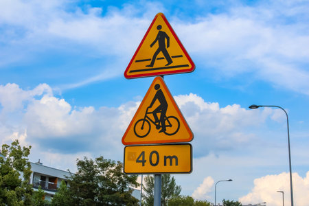 Orange warning road signs displaying bicycle prohibition symbols against cloudy blue sky