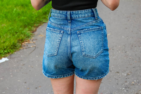 Young woman wearing casual denim shorts standing on grass showing summer fashion and lifestyle