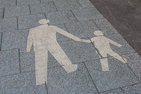 White painted pedestrian crossing symbols on dark asphalt road surface showing adult and child figuresの写真素材