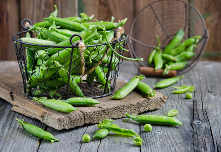 Fresh green peas in a basket on a wooden tableの写真素材